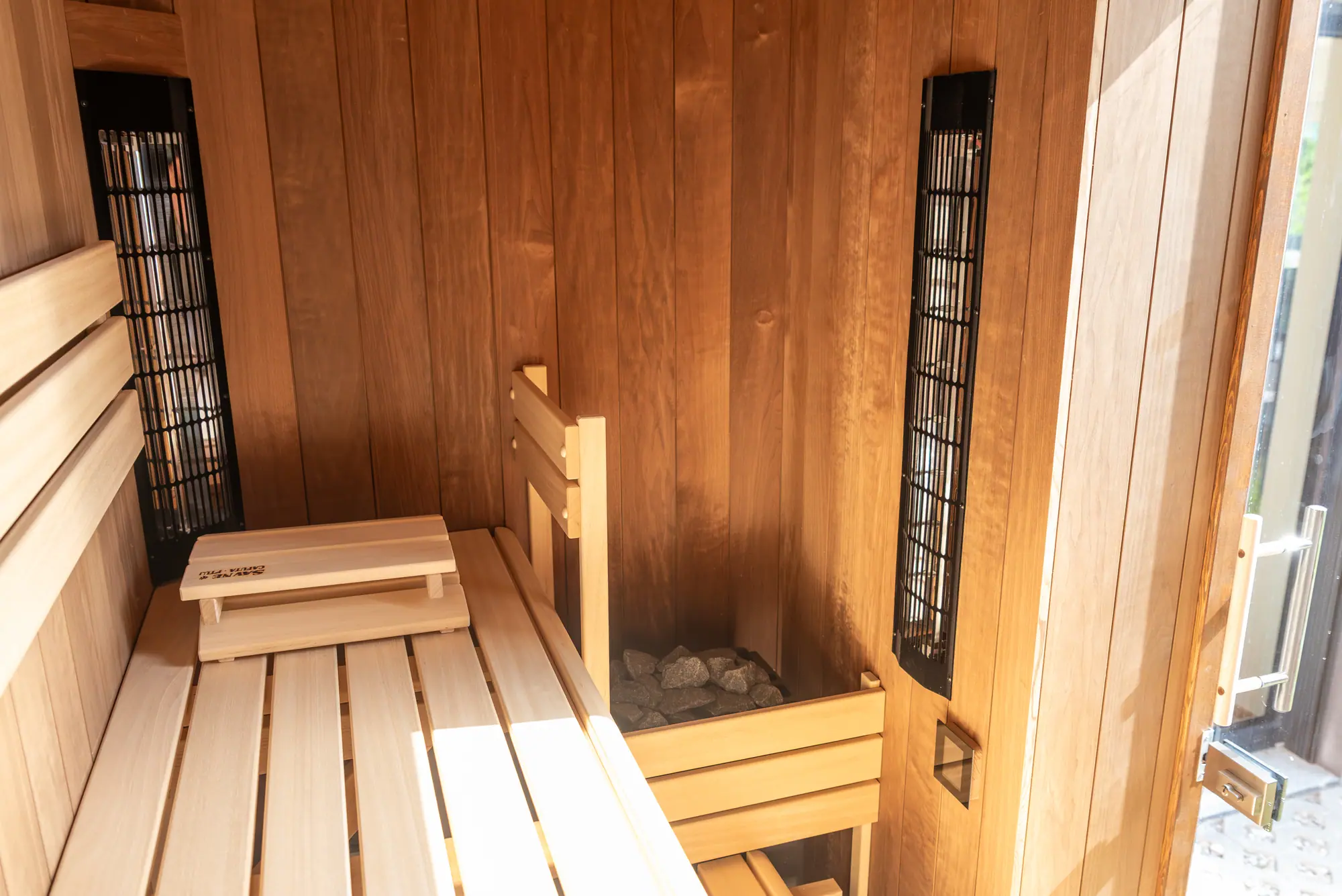 The sauna cabin — pale aspen benches, thermo-wood walls, and a stone heater